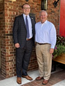 Two middle aged white men standing against a brick building